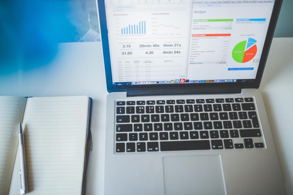A laptop showing charts and a dashboard, with a notebook beside it