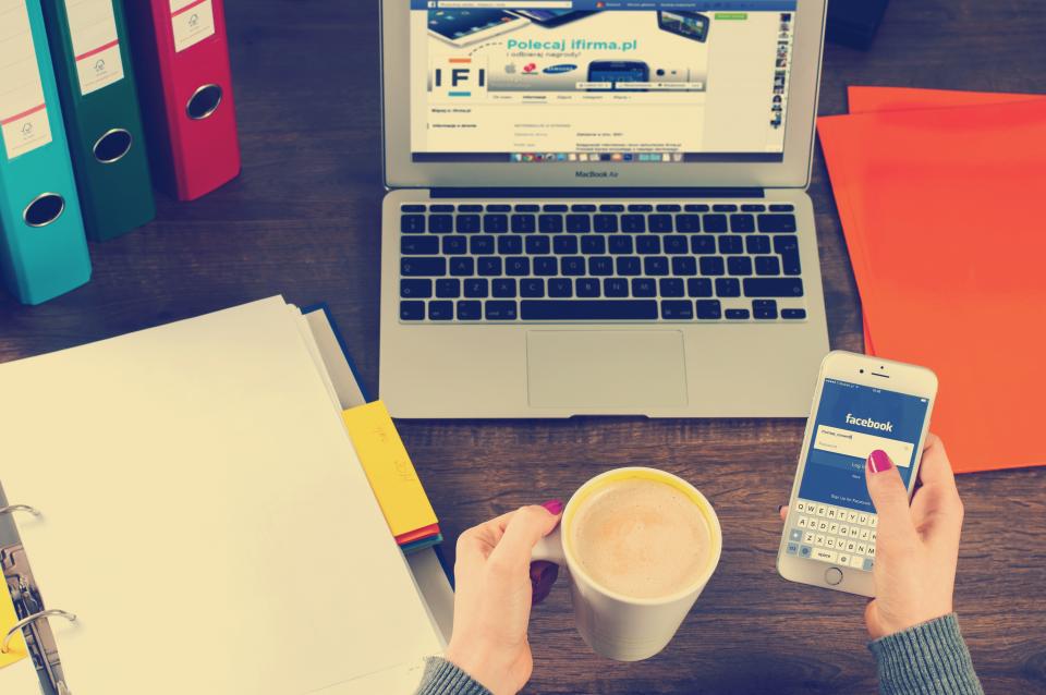 A person holding a phone beside a laptop and a coffee, seen from above